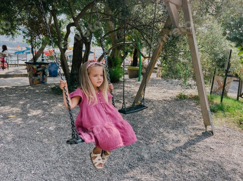 Preview: Little girl swings on a chain swing in the park among the trees