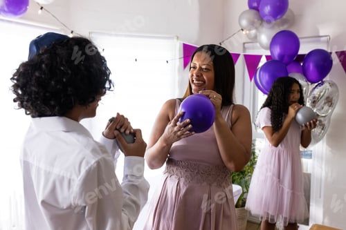 Preview: Celebrating religious event, family inflating colorful balloons together at home joyfully