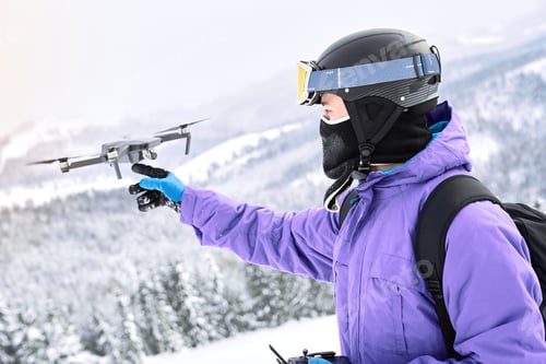 Preview: Male snowboarder with equipment and black backpack is launching a flying drone
