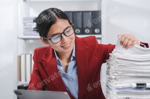 Preview: cheerful individual wearing glasses and a red blazer, hard working with large stack of papers