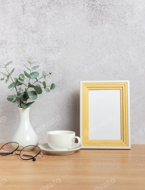 Preview: Eucalyptus branches, coffee cup, eyeglasses and empty photo frame creating cozy atmosphere on table