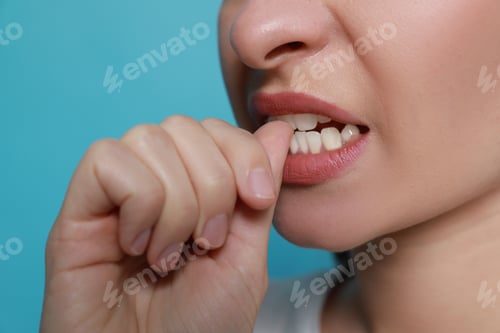 Preview: Young woman biting her nails on light blue background, closeup
