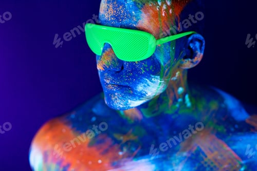 Preview: Young man shouts. Fluorescent paint on face and muscular torso, in studio shot with UV light