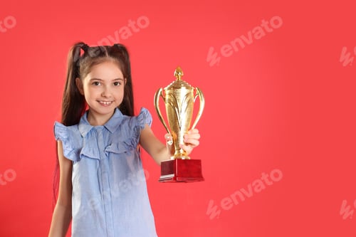 Preview: Happy girl with golden winning cup on red background. Space for text