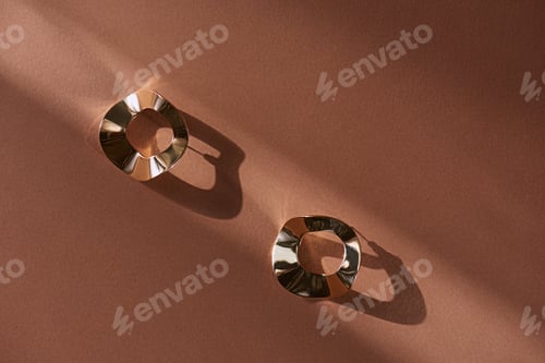 Preview: top view of beautiful luxury golden earrings on brown surface with sunlight
