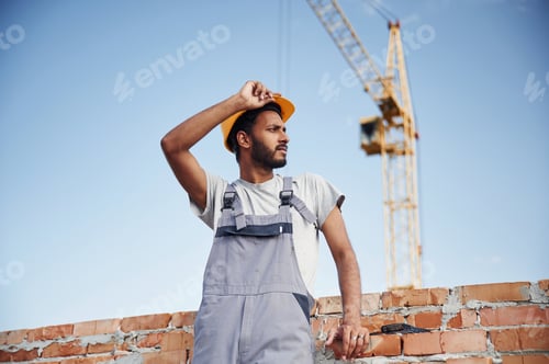 Preview: Standing against crane and blue sky. Handsome Indian man is on the construction site