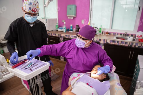 Preview: Mexican female dentist doing dental treatment on a young girl with the male assistant helping her