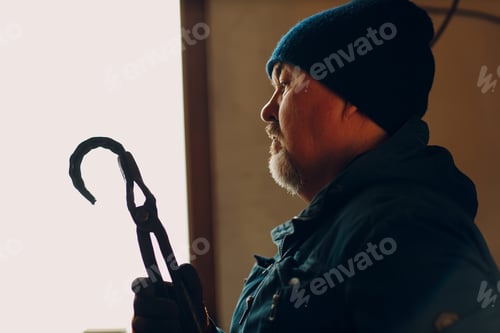 Preview: Blacksmith forges and checking tempered metal horseshoe in jar with water at forge.