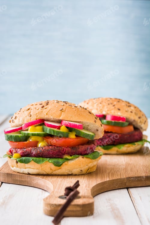 Preview: Two vegan burgers with beetroot cutlets resting on wooden chopping board