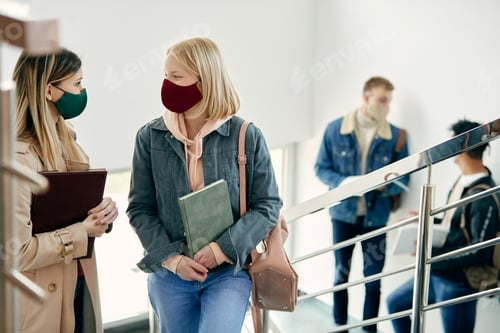 Preview: Young women with face masks talking while attending university classes during COVID-19 pandemic.