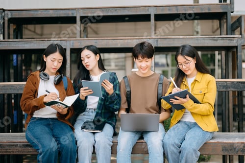 Preview: Young people college students is reading a book while relaxing sitting on grass in a campus park