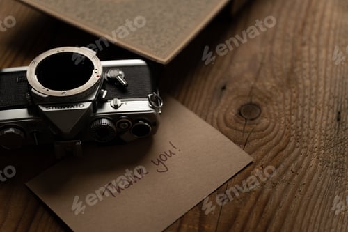 Preview: Retro analog camera, old brown book and postcard saying Thank you on a wooden table