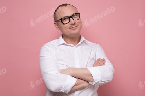 Preview: Smiling mature man in glasses and white shirt standing with folded hands