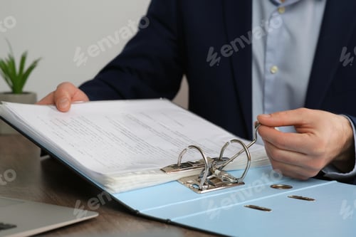 Preview: Businessman putting document into file folder at wooden table in office, closeup