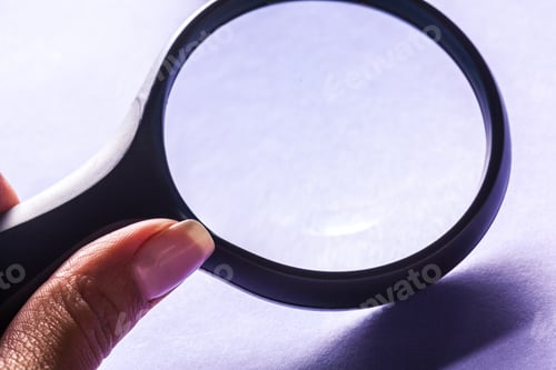 Preview: Hand holding magnifying glass on purple background with soft shadows in focus