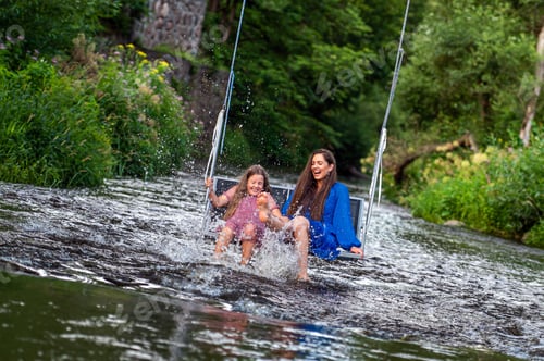 Preview: a woman and a young girl are swinging across a fast-flowing river, laughing and splashing with water