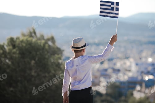 Preview: Smiling baby toddler, boy holding a Greece flag on city background. Independence Day, Flag Day.