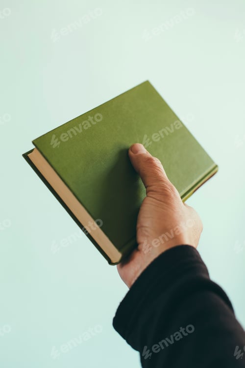 Preview: A man's hand holding an old green hardback book.