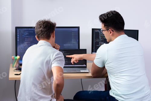 Preview: Programmers looking for bugs in the code together on a computer with three monitors.