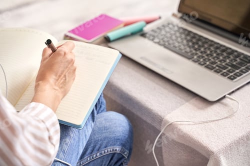 Preview: Woman taking notes in notebook with laptop and colorful notebooks on table
