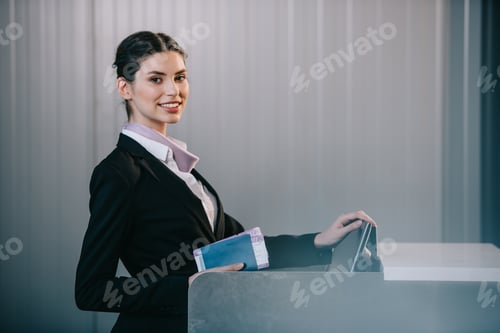 Preview: young female worker smiling at camera while working at check-in desk in airport