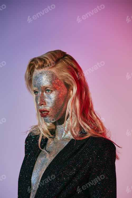 Preview: portrait of expressive blonde woman with glitter makeup and sparkling dress posing on pink gradient