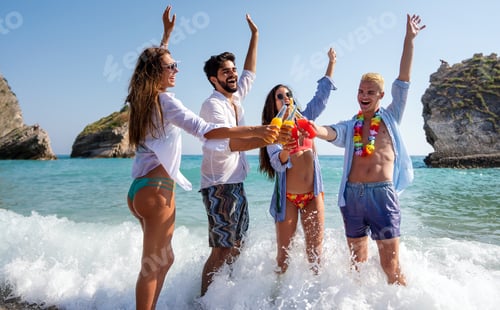 Preview: Group of young friends having fun at the beach with colorful drinks, laughing in the sun at summer