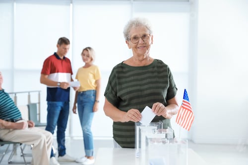 Preview: Elderly woman putting ballot paper into box at polling station