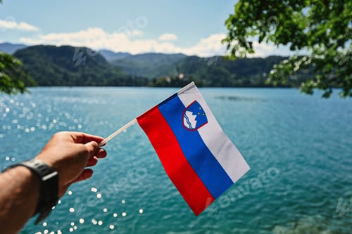 Preview: Man hand hold slovenian flag against view of beautiful Bled Lake, Slovenia.