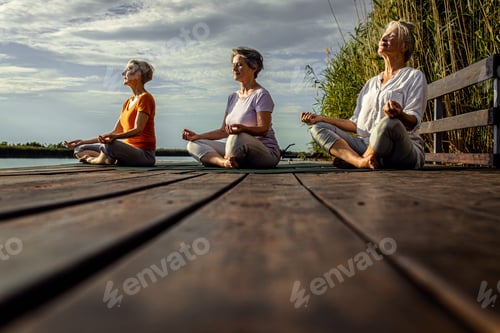 Preview: Group of senior woman doing yoga exercises by the lake.