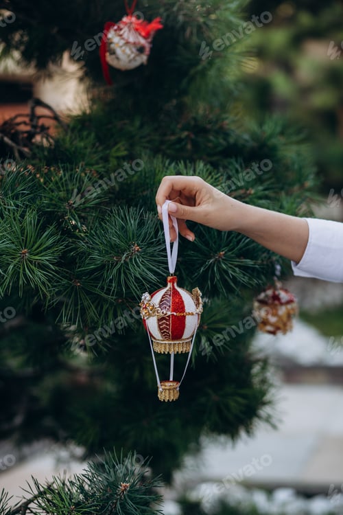 Preview: Merry Christmas and Happy New Year. Women's hands decorate the Christmas tree with balls and toys.