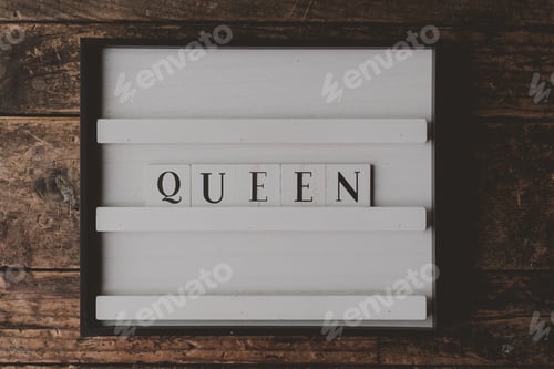 Preview: White sign with a writing Queen on it on a wooden brown background