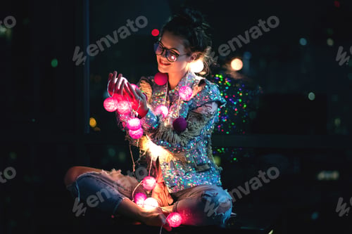 Preview: Happy woman wearing glowing jacket with sequins is holding light balls in her hands