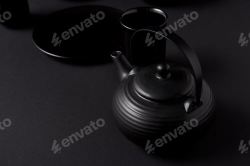 Preview: selective focus of black teapot, cups and plate on black table