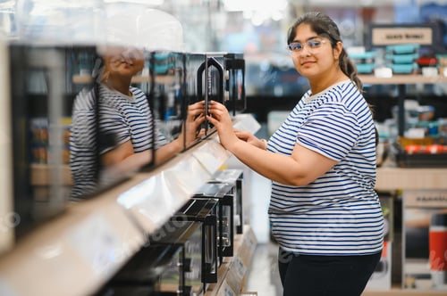 Preview: Indian Woman shopping for microwave in appliances store.