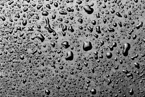 Preview: Water droplets on a dark surface reflect light in an abstract pattern