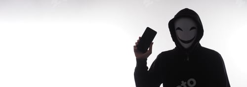 Preview: Hacker Anonymous and face mask with smartphone in hand.