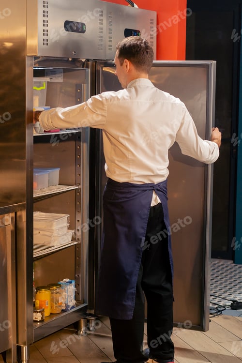 Preview: professional kitchen chef looks into the fridge and chooses ingredients for cooking food concept