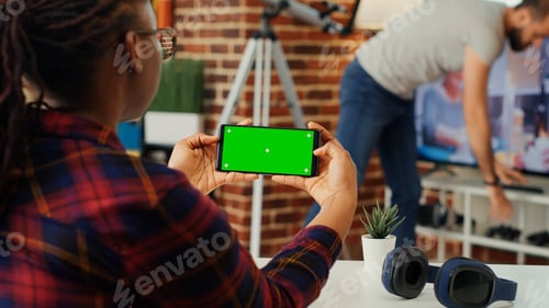 Preview: Female worker looking at horizontal greenscreen on smartphone