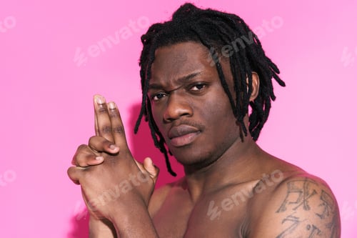 Vista previa: Black shirtless man with dreadlocks frowning while making gun gesture