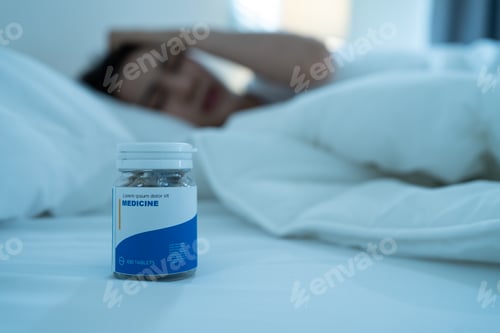 Preview: Close up of medicine pills bottle on bed with sleeping sickness woman.