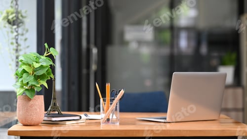 Preview: Wooden office desk with laptop computer, notebooks, pencil holder and potted plant.
