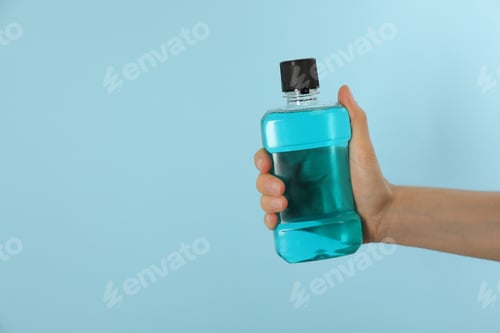 Preview: Woman holding bottle with mouthwash on light blue background, closeup. Space for text