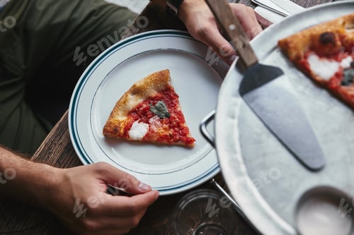 Preview: cropped shot of man eating delicious pizza margherita at restaurant