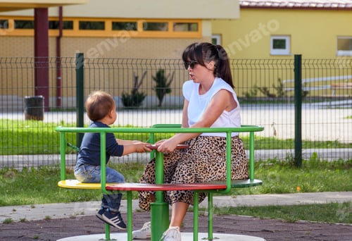 Preview: Young mother and her child on a carousel on playground in park