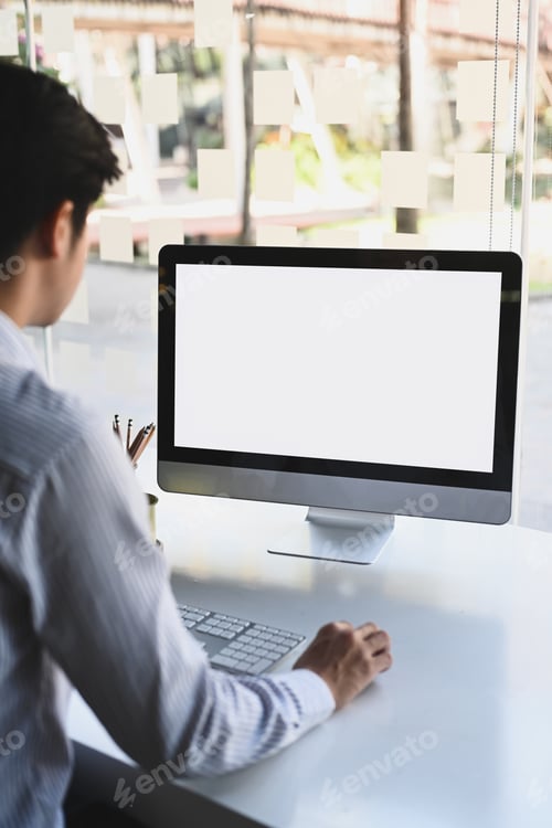 Preview: Rear view of businessman working with computer while sitting in modern office.