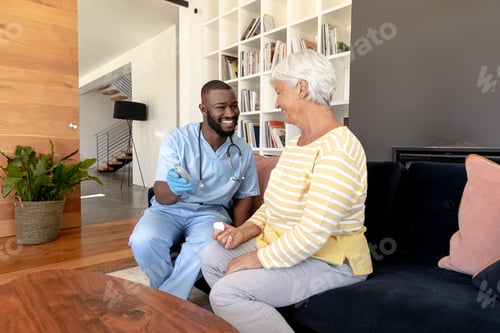 Preview: African american male health worker measuring blood sugar of caucasian senior woman using glucometer