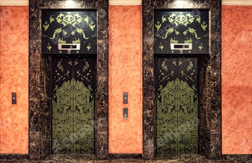 Preview: Vintage asian carved brass two elevator door on orange marble wall in the hotel