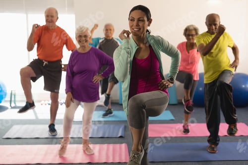 Preview: Front view of young female trainer assisting senior people in fitness studio