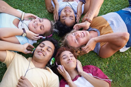 Preview: High angle of a group of friends lying on their backs on the grass in a park and listening to music